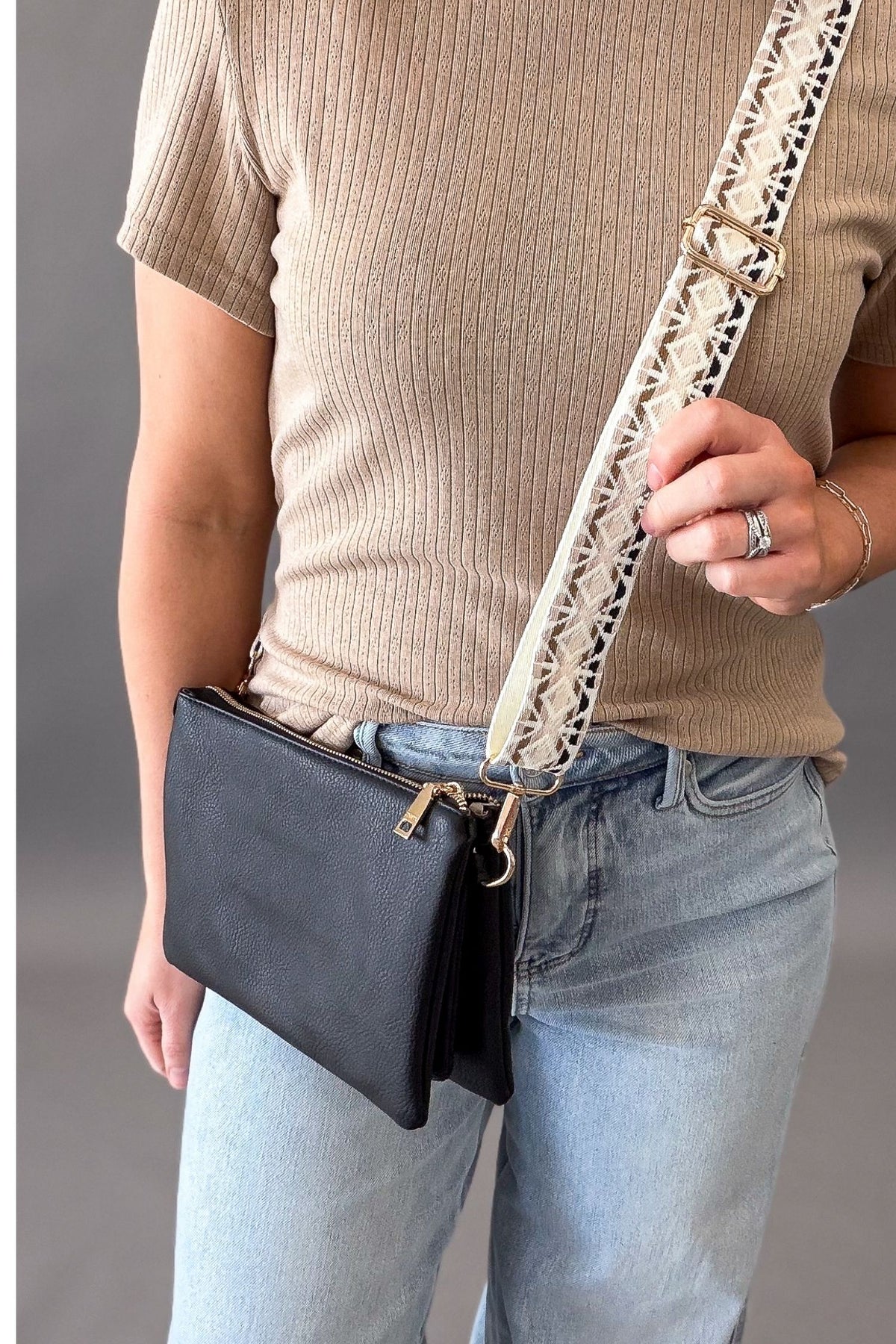Person wearing a beige sweater and blue jeans with a black handbag and neutral textured guitar strap.