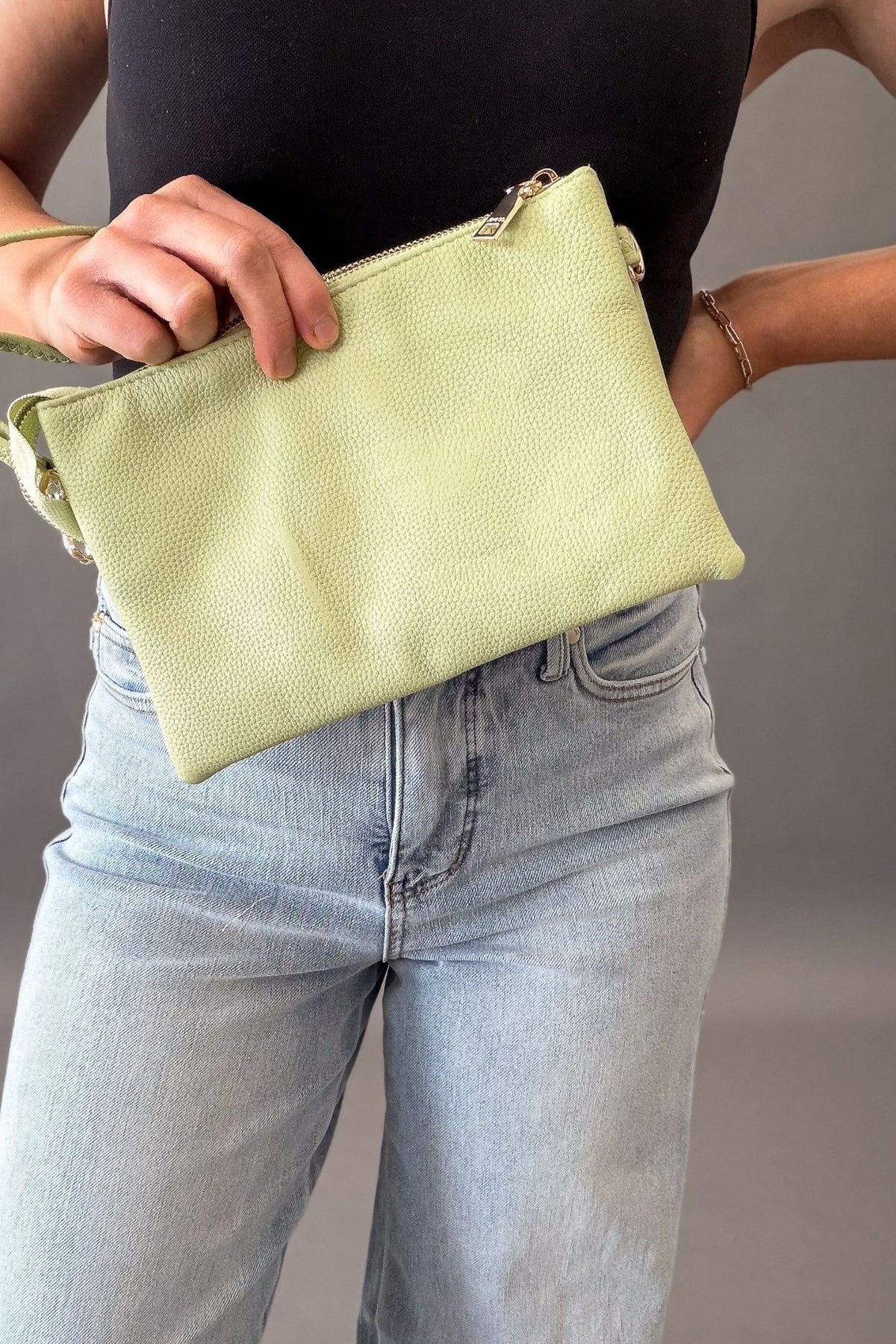 Person holding a light green clutch bag with a neutral background