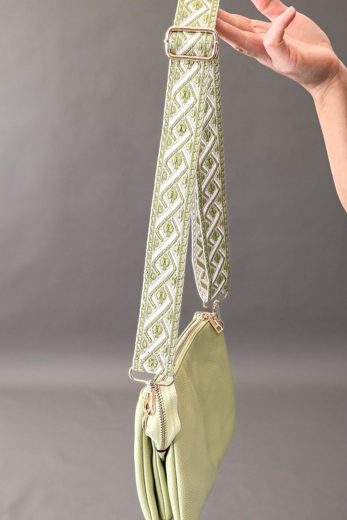 Light green handbag with decorative strap held by a hand against a gray background