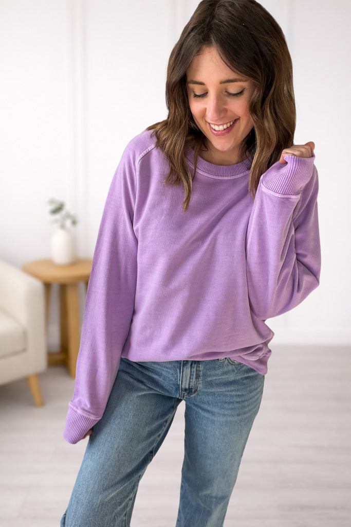Woman wearing a lavender sweatshirt and blue jeans indoors.