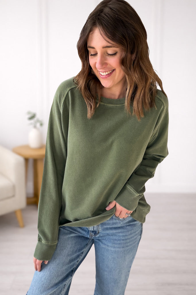 Woman wearing a green sweater and blue jeans indoors.