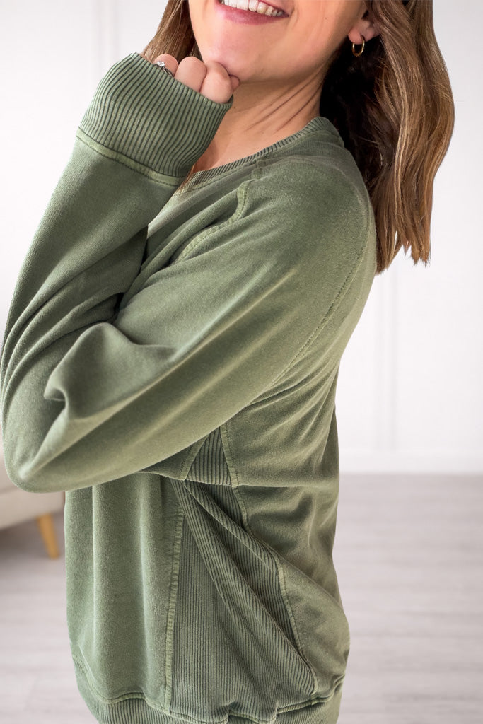Person wearing a green sweatshirt showing ribbed accents on the side with a blurred background