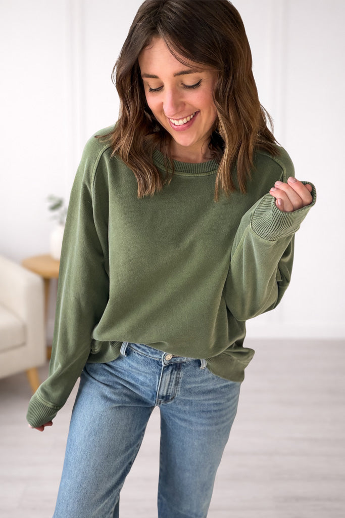 Woman wearing a green sweater and blue jeans indoors.