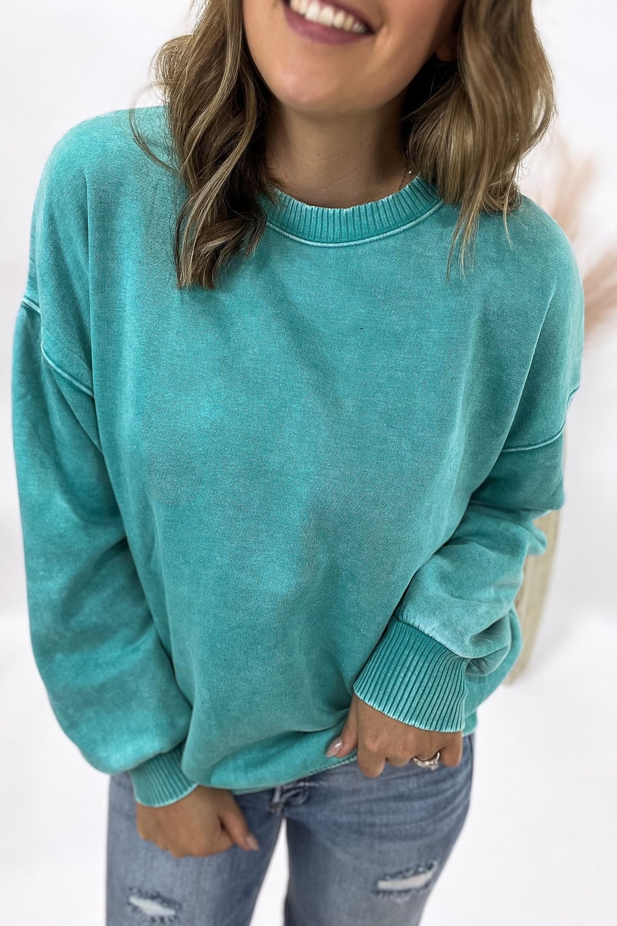 Person wearing a teal sweater and jeans against a white background
