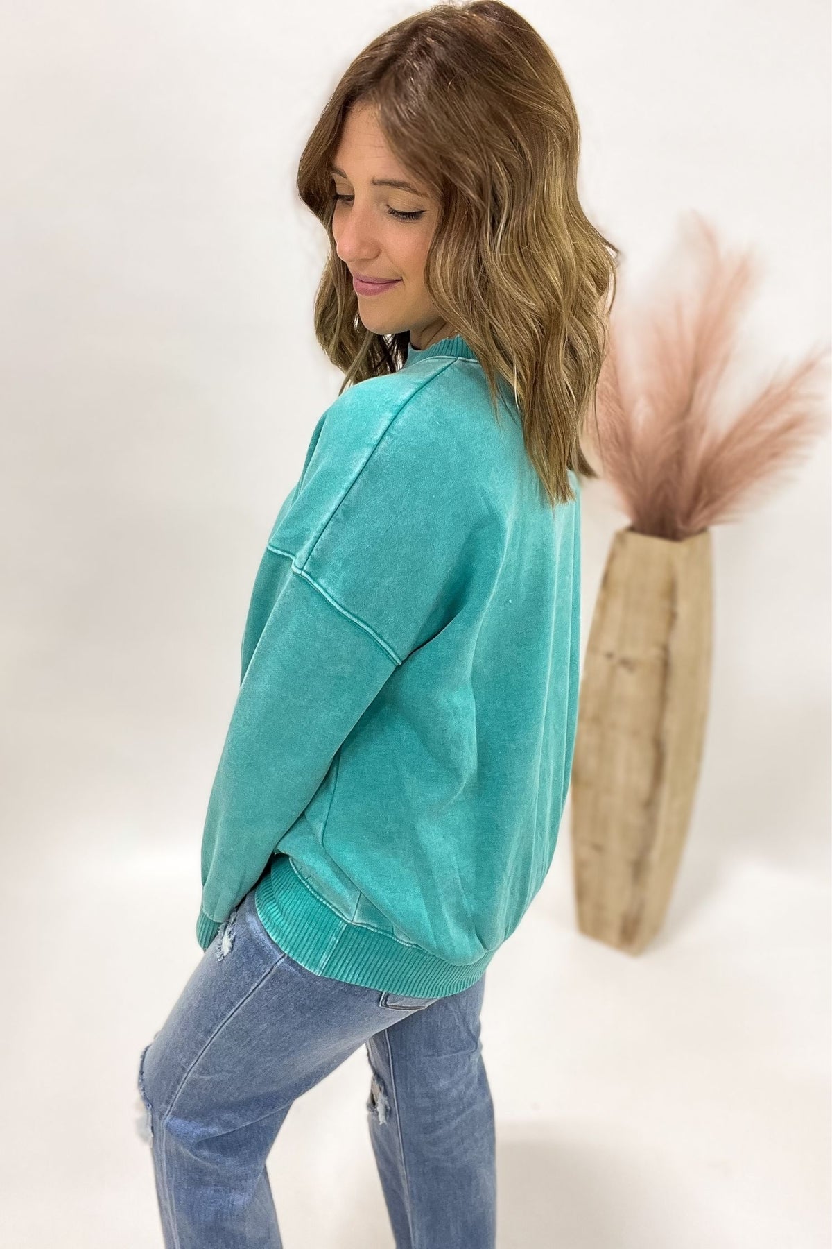 Woman wearing a teal sweater and blue jeans against a white background