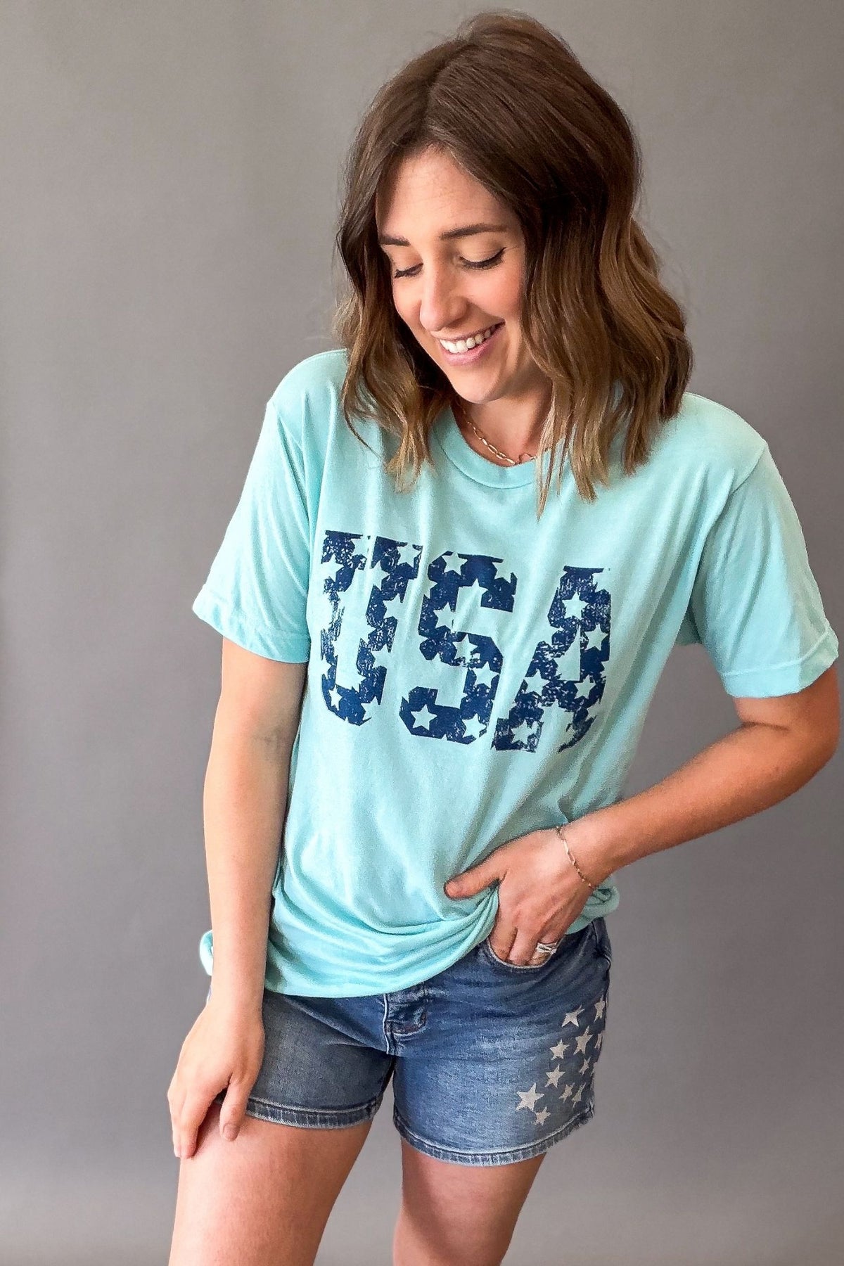 Woman wearing a light blue t-shirt with 'USA' printed in navy, standing against a plain background