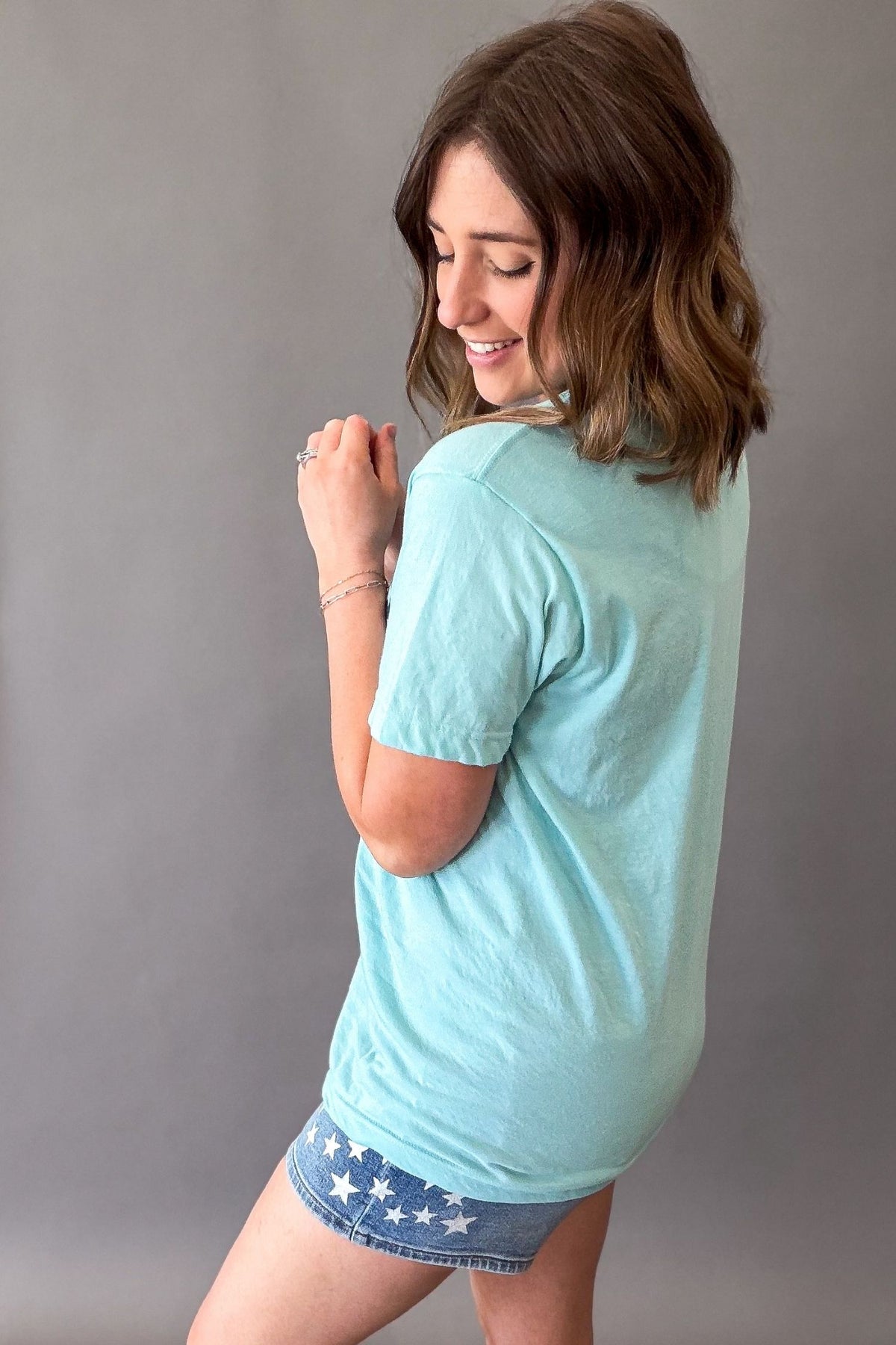 Woman wearing a light blue t-shirt and denim shorts with white star pattern against a gray background