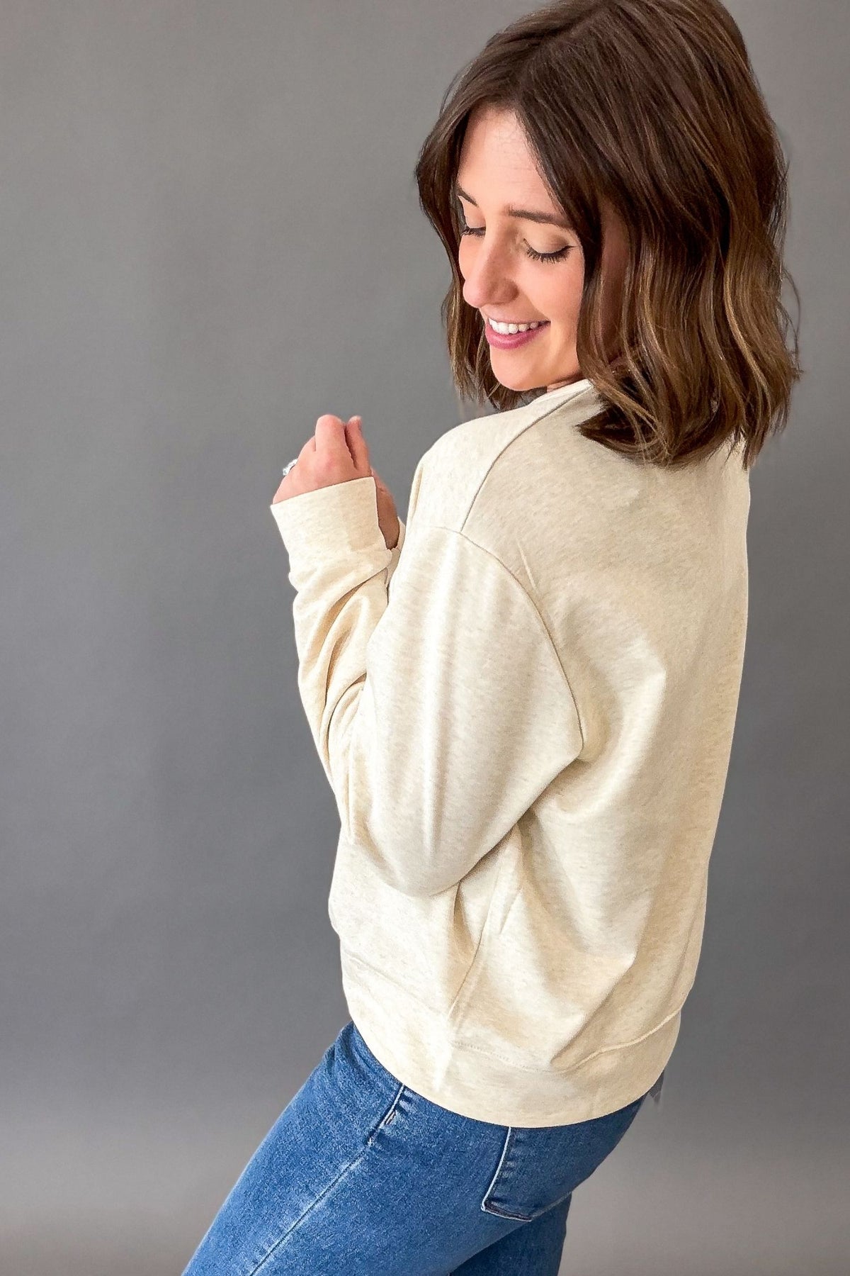 Women's heathered warm taupe USA sweatshirt featuring white eyelet appliqué lettering, crew neckline, drop shoulders, and a relaxed fit paired with denim.