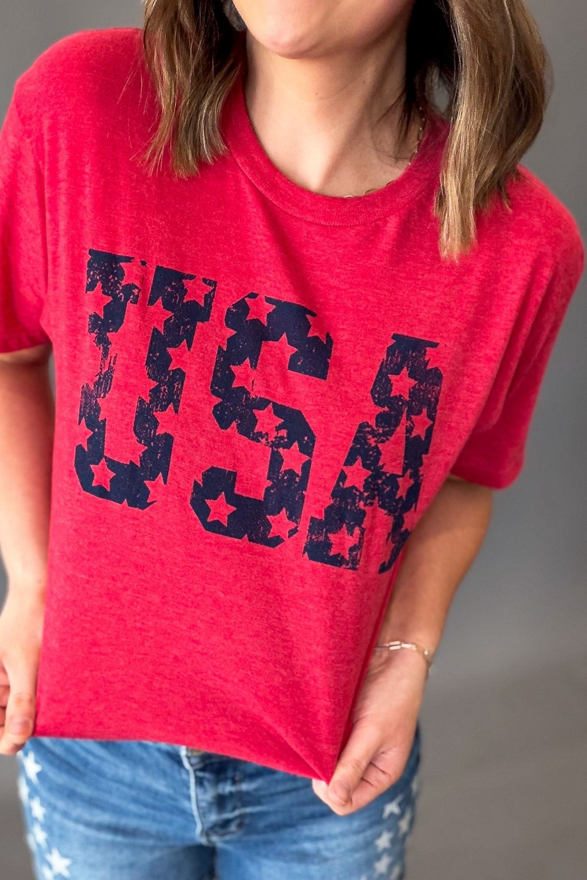 woman wearing a heather red solid tee with a navy screen printed USA graphic with stars