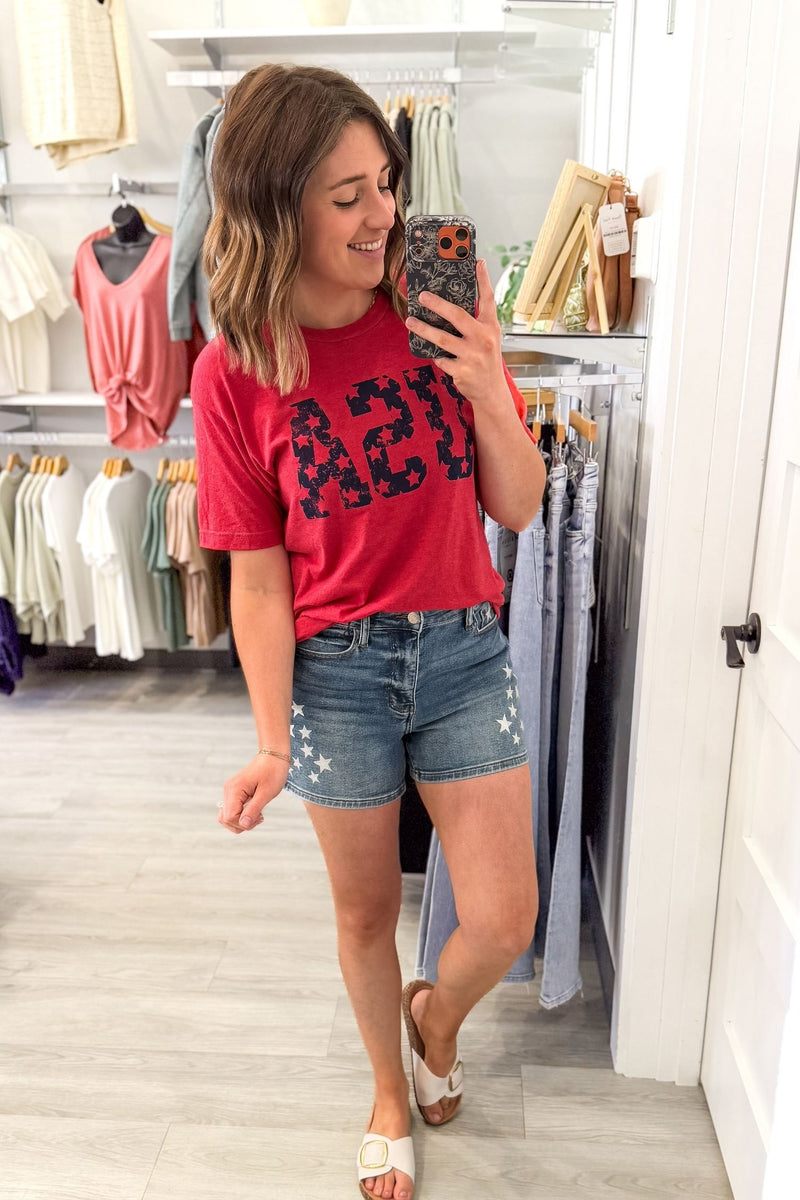 woman taking a mirror selfie wearing an easy forth of july graphic tee paired with judy blue star shorts and white sandals