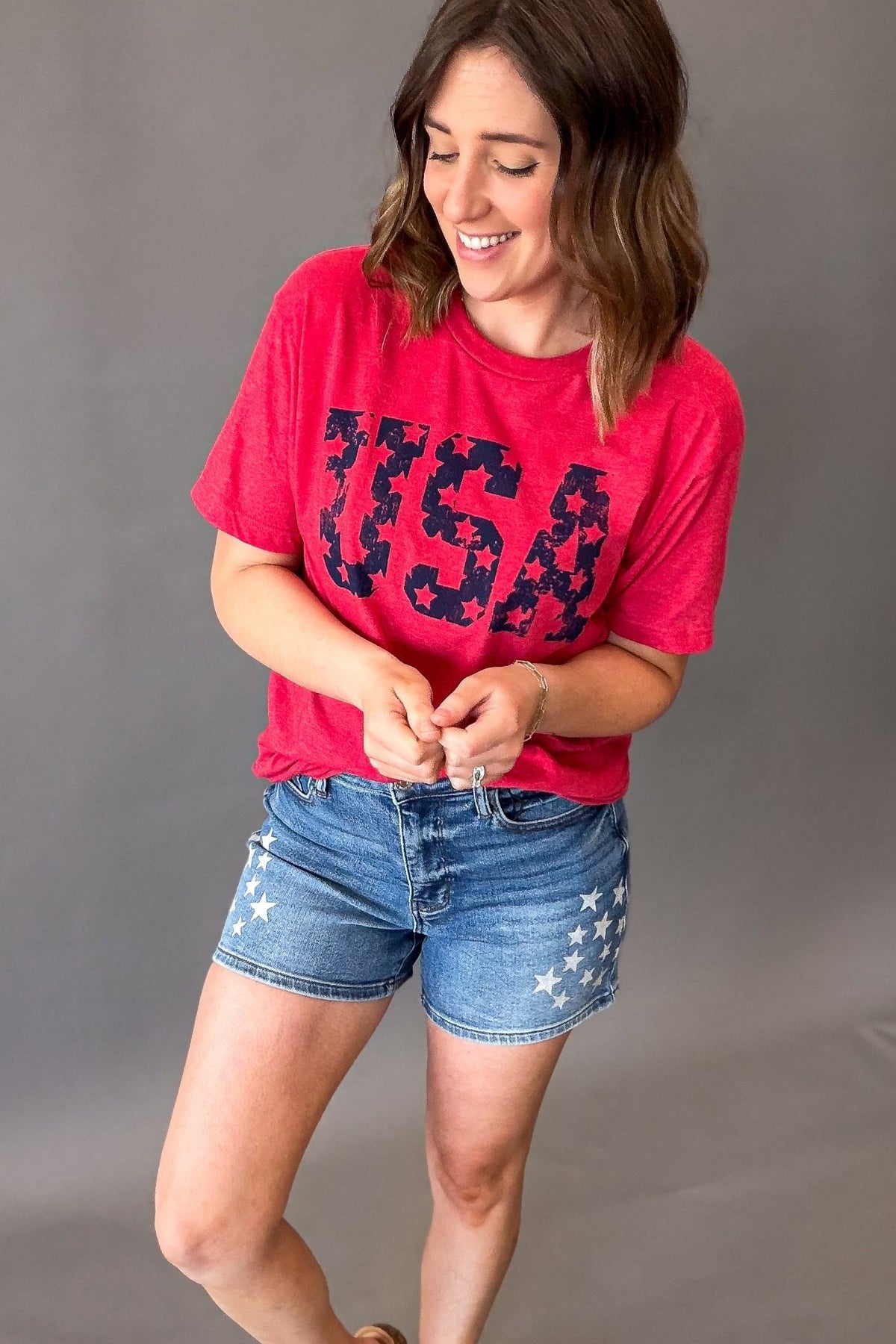 woman wearing a red usa graphic short sleeve top with judy blue star shorts on a grey background