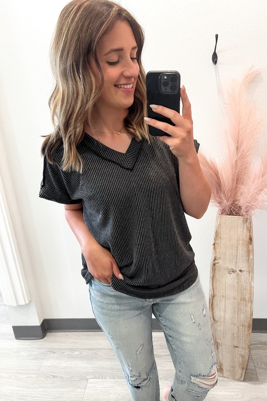 Woman taking a selfie wearing a charcoal textured top and light blue jeans, standing indoors.