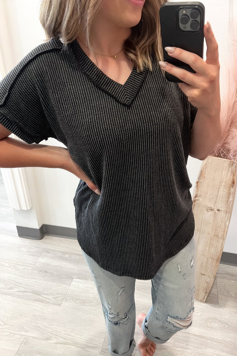 Person wearing a charcoal ribbed tee and light blue jeans, taking a mirror selfie.