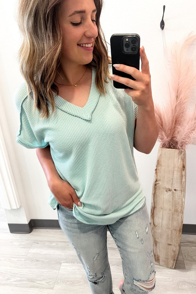 Woman taking a mirror selfie wearing a light green sweater and ripped jeans.