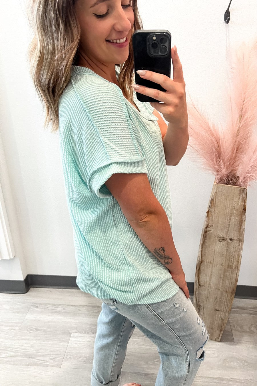 Woman taking a selfie wearing a light mint short sleeve and jeans, standing indoors.