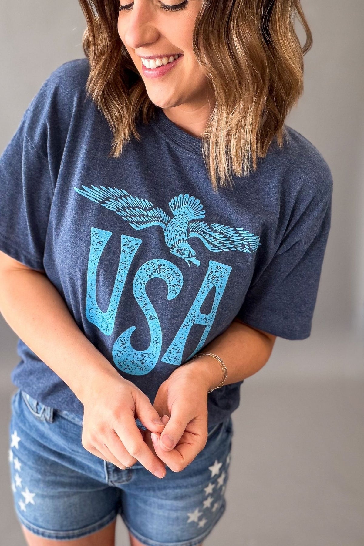 Woman wearing a navy vintage USA eagle graphic tee with distressed light blue screen printed graphic and denim shorts