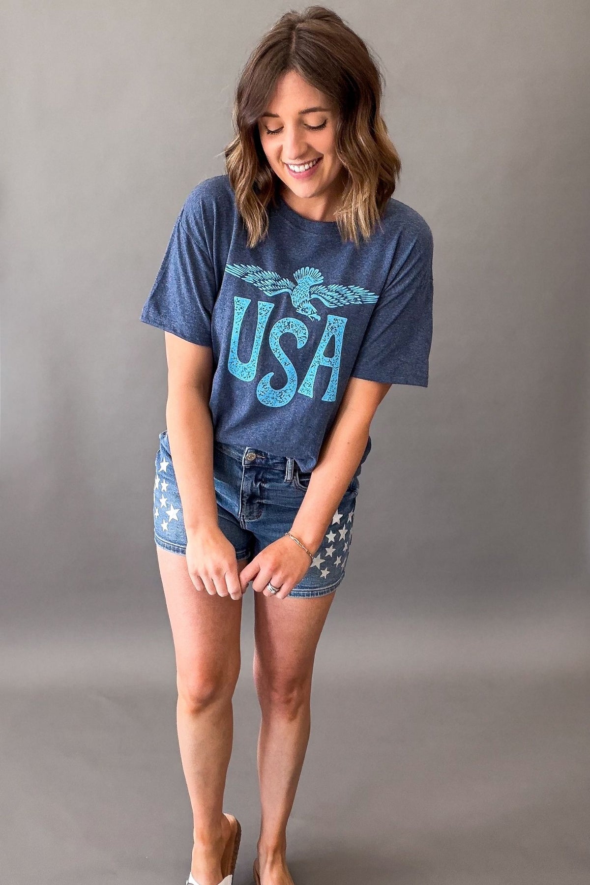 Woman wearing a navy vintage USA eagle graphic tee with distressed light blue screen printed graphic and denim shorts