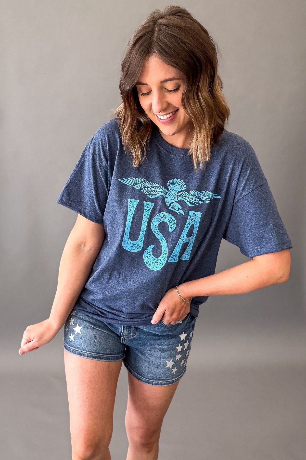 Woman wearing a navy vintage USA eagle graphic tee with distressed light blue screen printed graphic and denim shorts