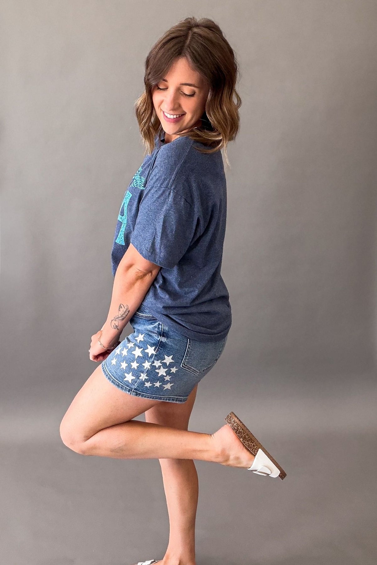 Woman wearing a navy vintage USA eagle graphic tee with distressed light blue screen printed graphic and denim shorts showing the side details