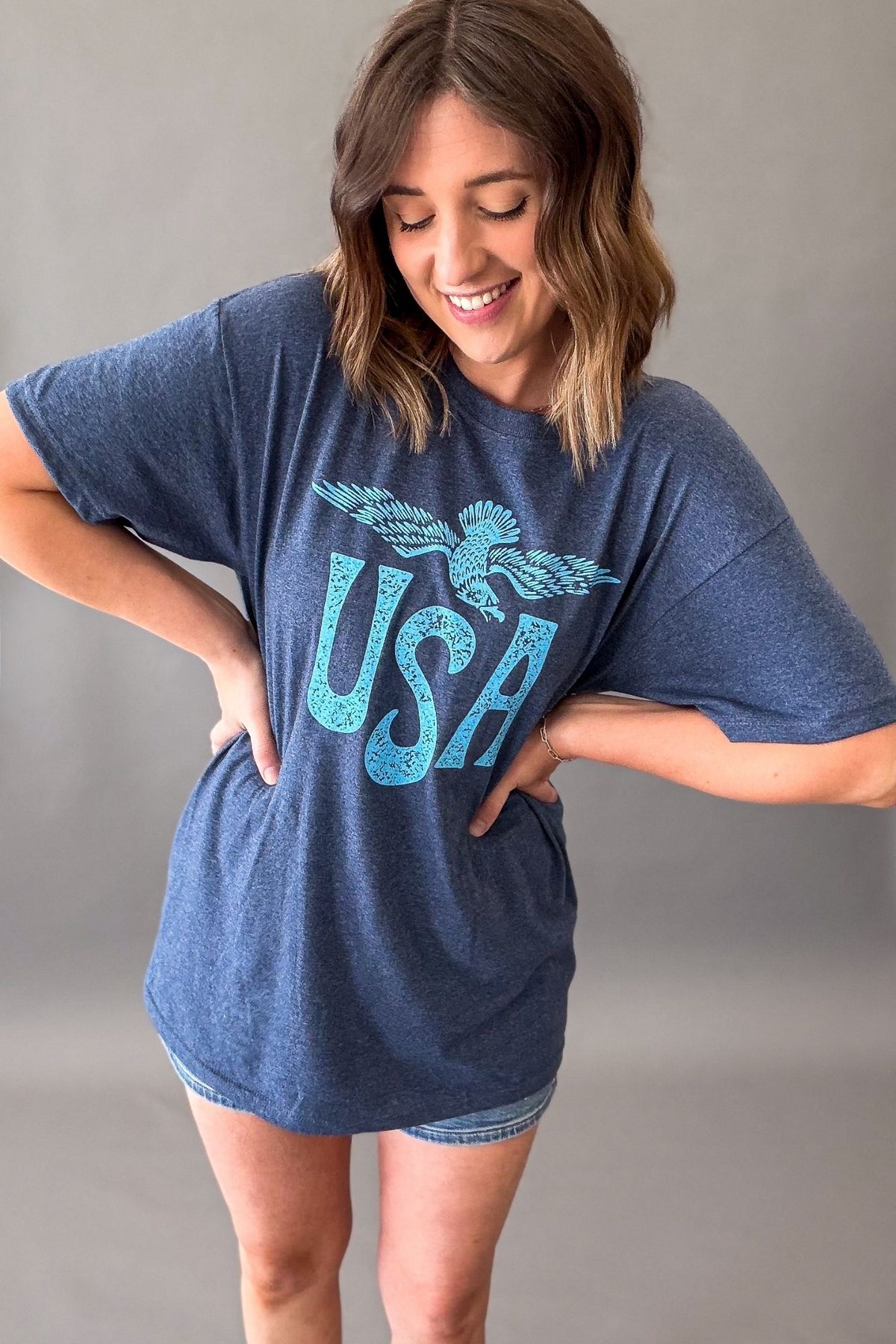 Woman wearing a navy vintage USA eagle graphic tee with distressed light blue screen printed graphic and denim shorts showing the tee length