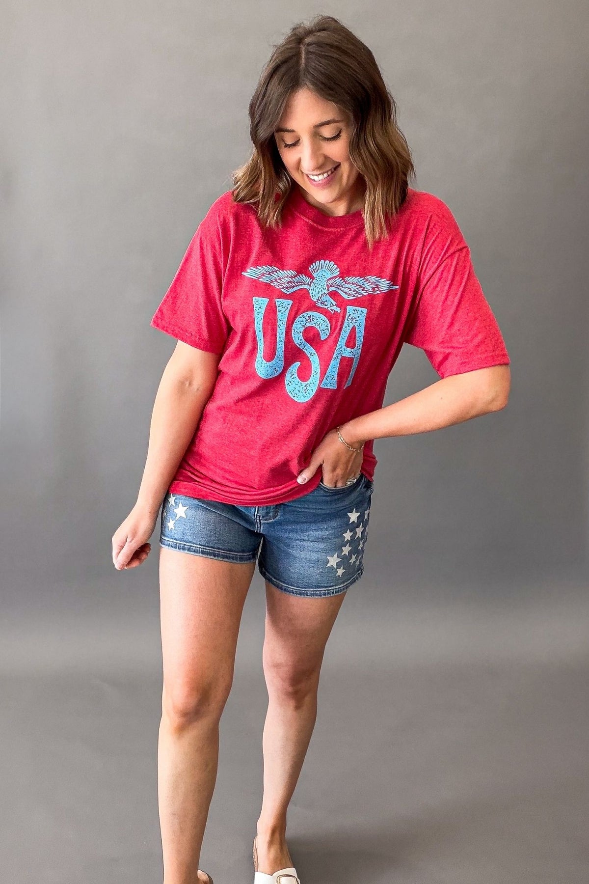 Woman wearing a red vintage USA eagle graphic tee with distressed light blue screen printed graphic and denim shorts