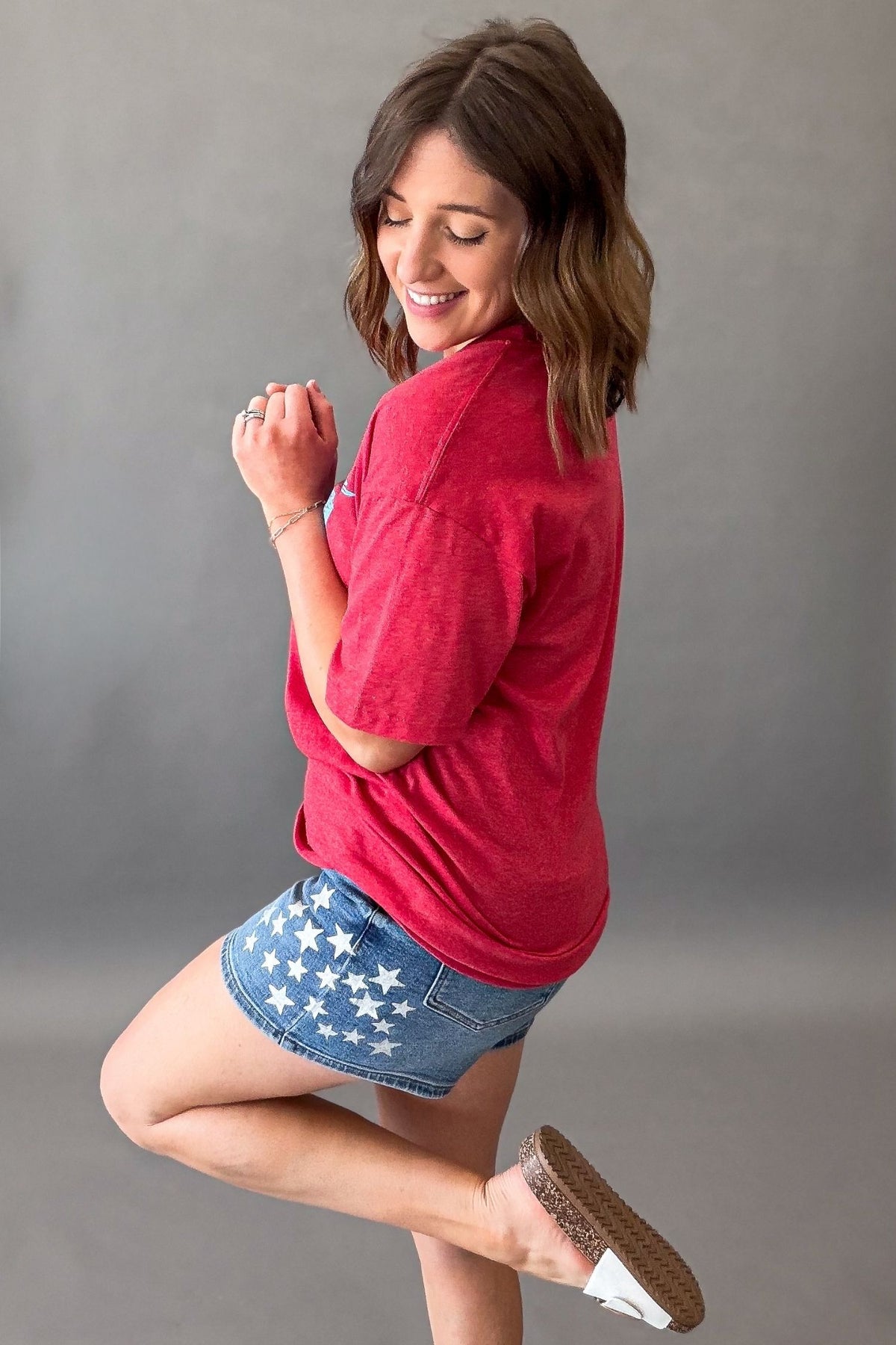 Woman wearing a red vintage USA eagle graphic tee with distressed light blue screen printed graphic and denim shorts showing the blank side details of the tee