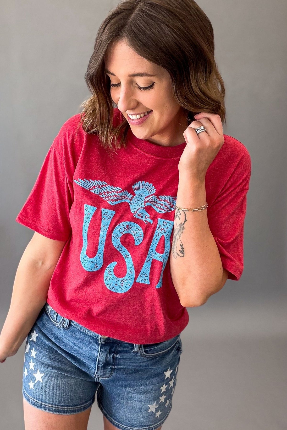 Woman wearing a red vintage USA eagle graphic tee with distressed light blue screen printed graphic and denim shorts