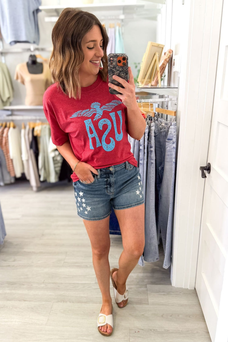 Woman taking a selfie wearing a red vintage USA eagle graphic tee with distressed light blue screen printed graphic and denim shorts