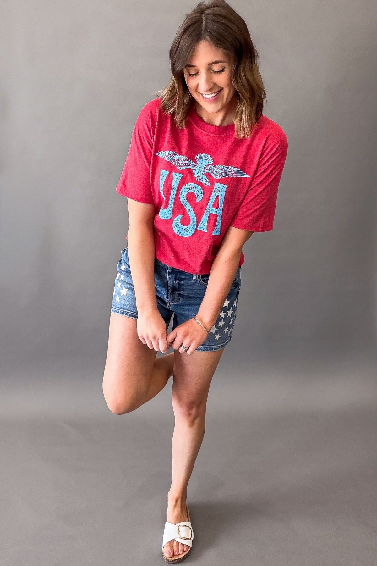 Woman wearing a red vintage USA eagle graphic tee with distressed light blue screen printed graphic and denim shorts