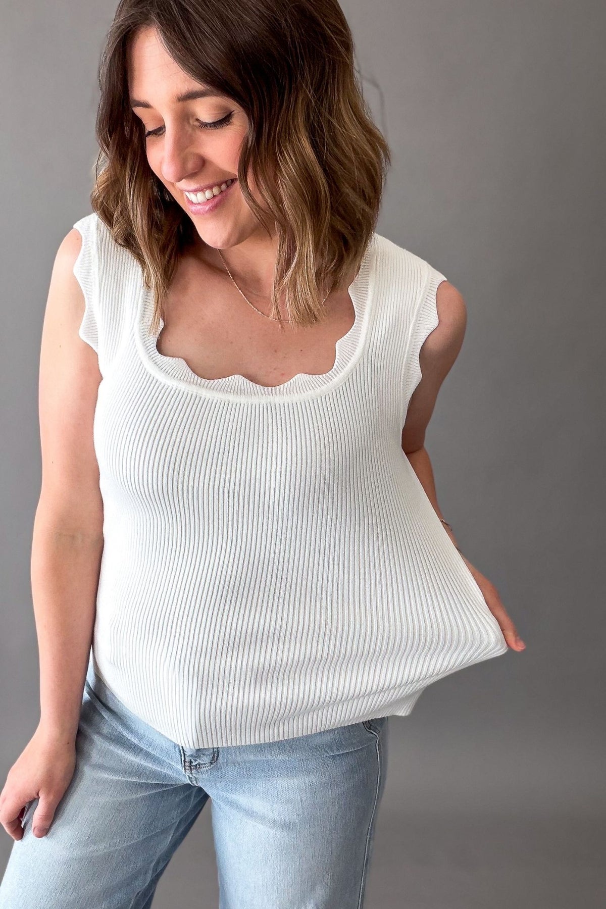 Woman wearing a white sleeveless top and light blue jeans against a gray background