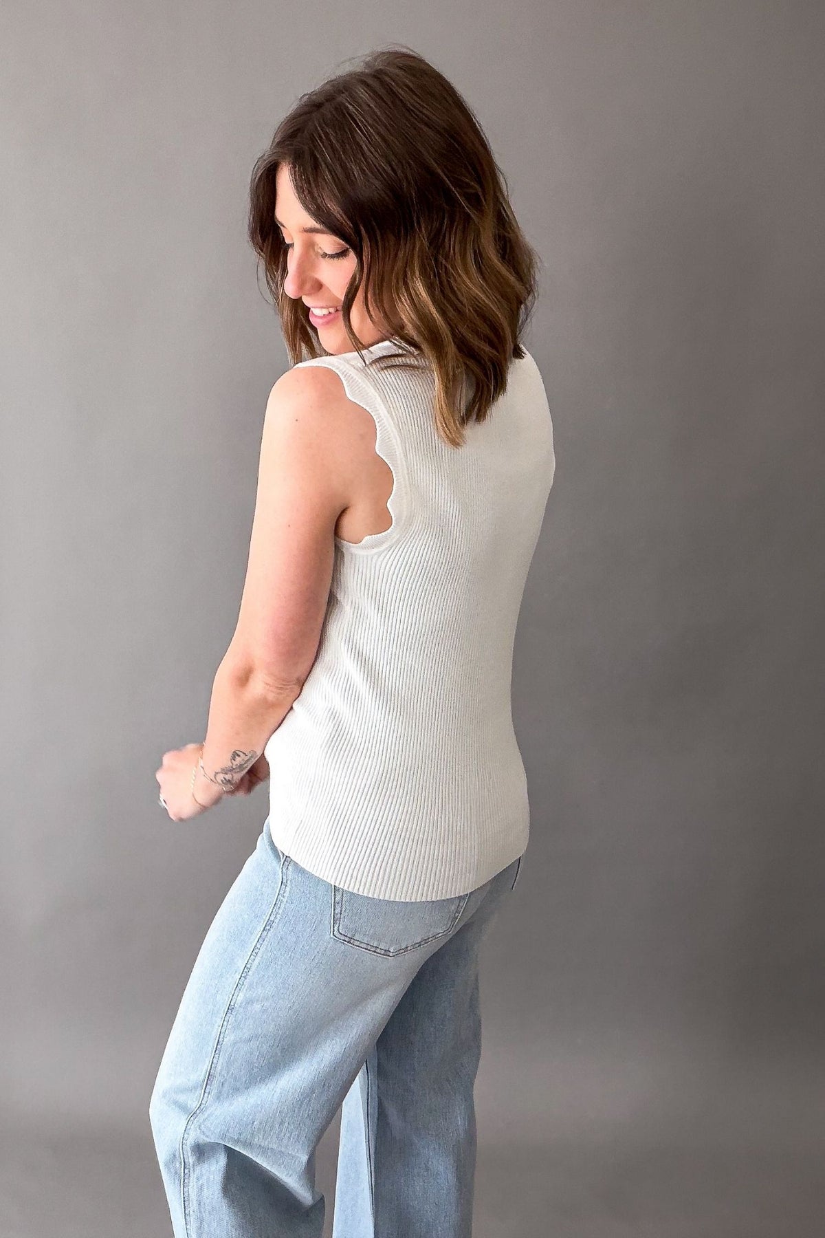 Woman wearing a white sleeveless top and light blue jeans against a gray background