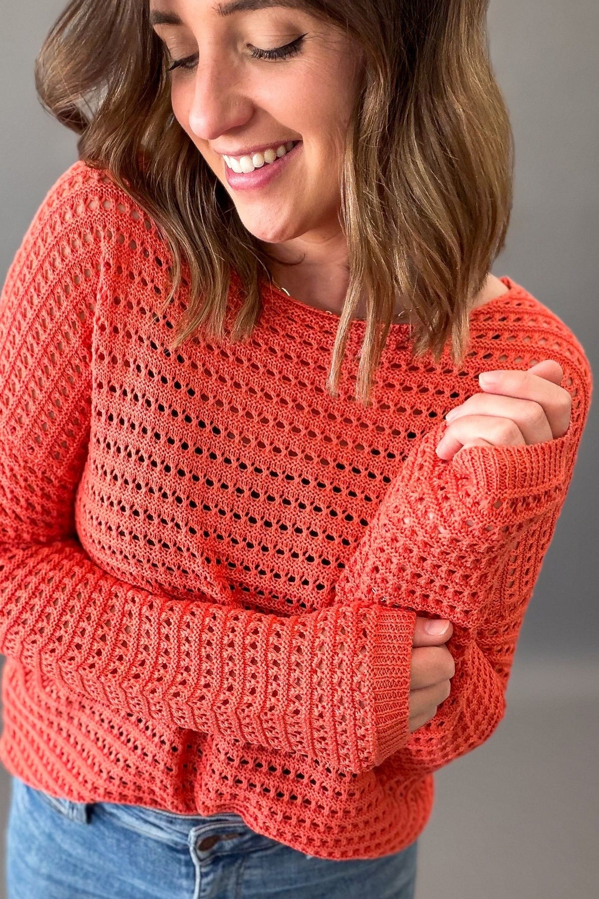 woman wearing a beachy orange knit pullover and blue jeans on a charcoal background