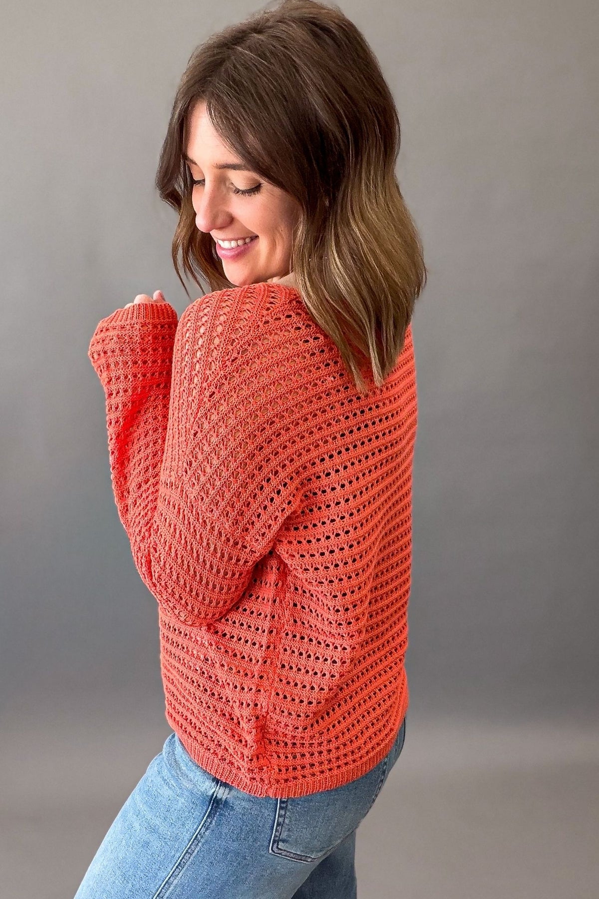 woman wearing an orange crochet knit light weight long sleeve and blue jeans showing the sides and back details