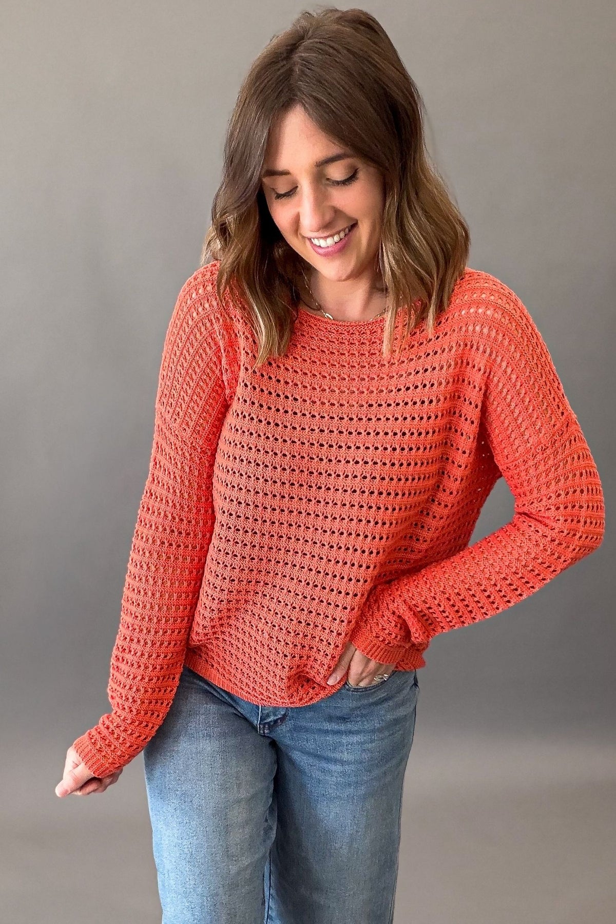 woman wearing an orange crochet sweater paired with blue jeans on a charcoal background