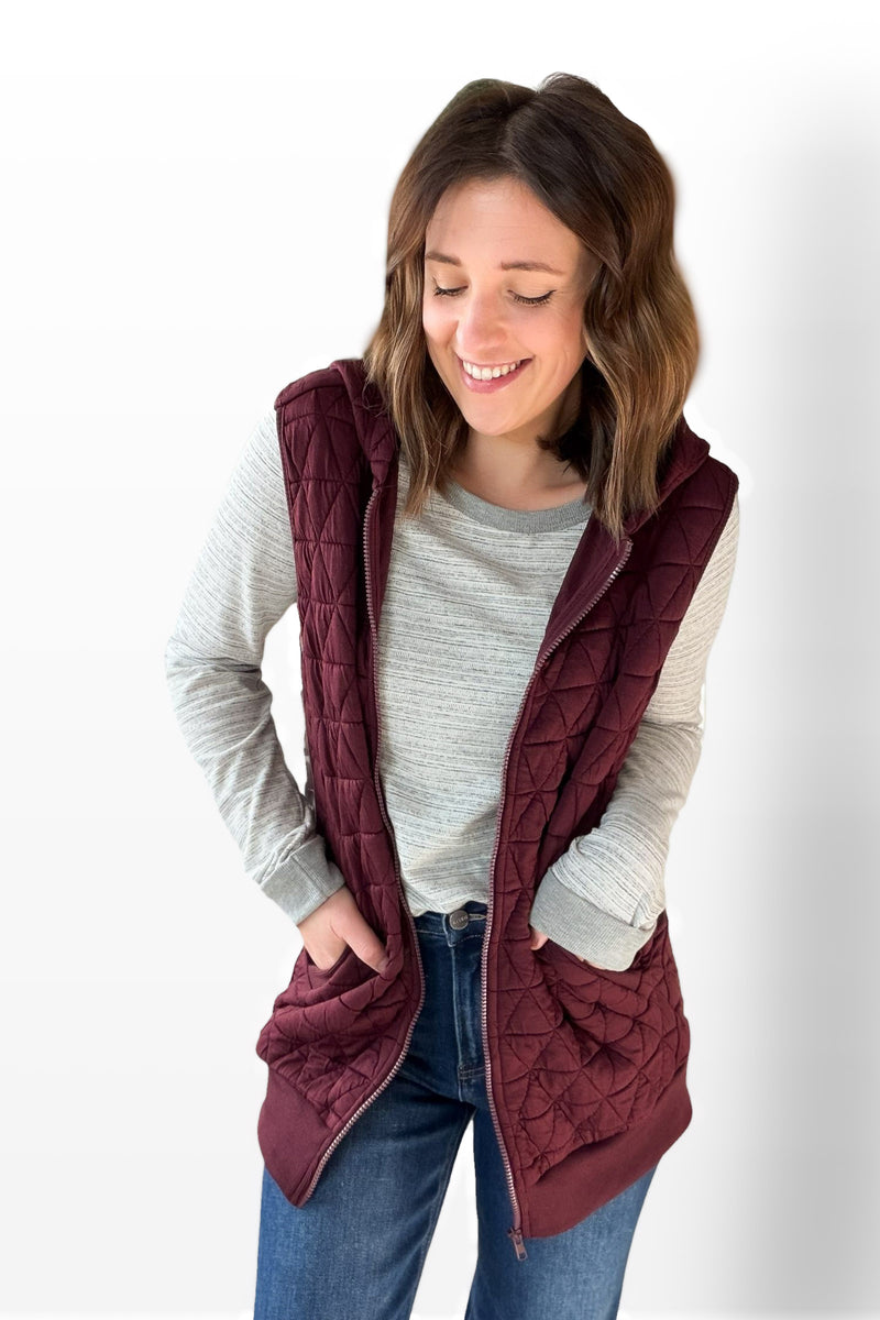 Woman wearing a wine quilted vest over a gray sweater on a white background