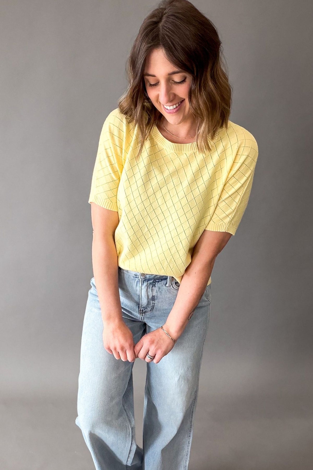 Woman wearing a yellow pointelle short sleeve and light blue jeans against a gray background