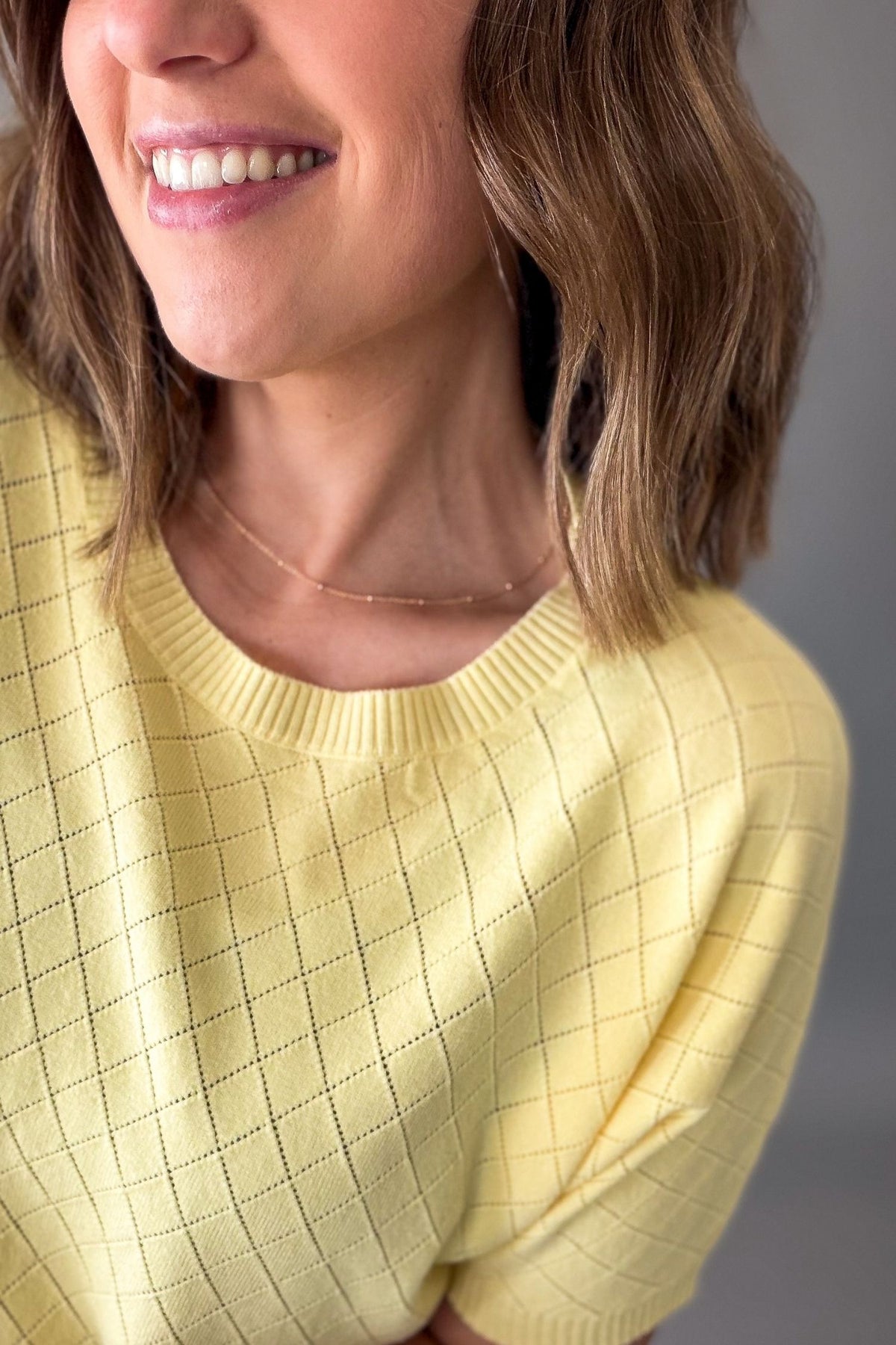 Woman wearing a yellow knit short sleeve against a gray background