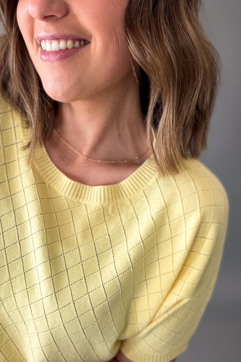 Woman wearing a yellow knit short sleeve against a gray background