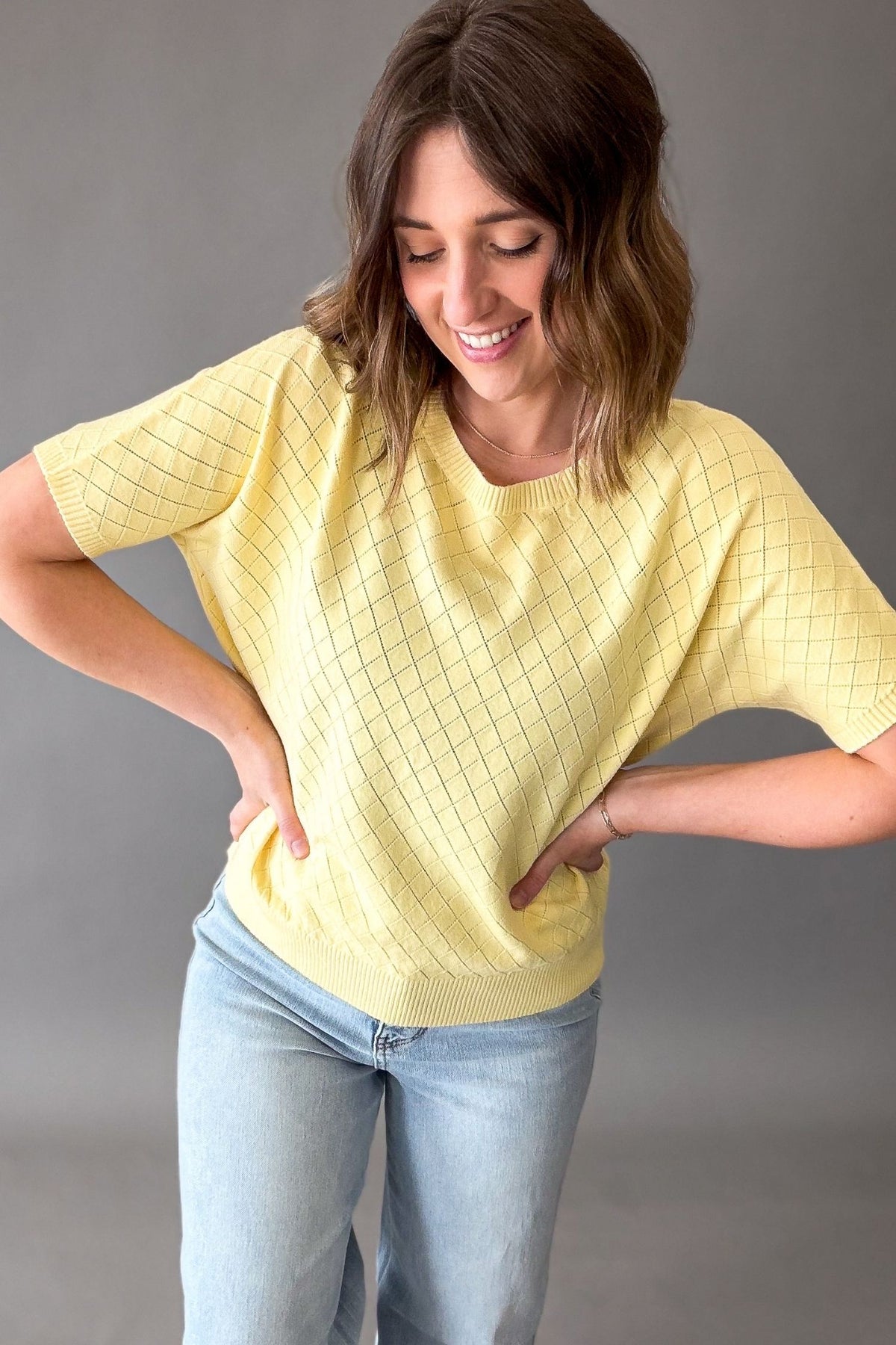 Woman wearing a yellow textured top and light blue jeans against a gray background