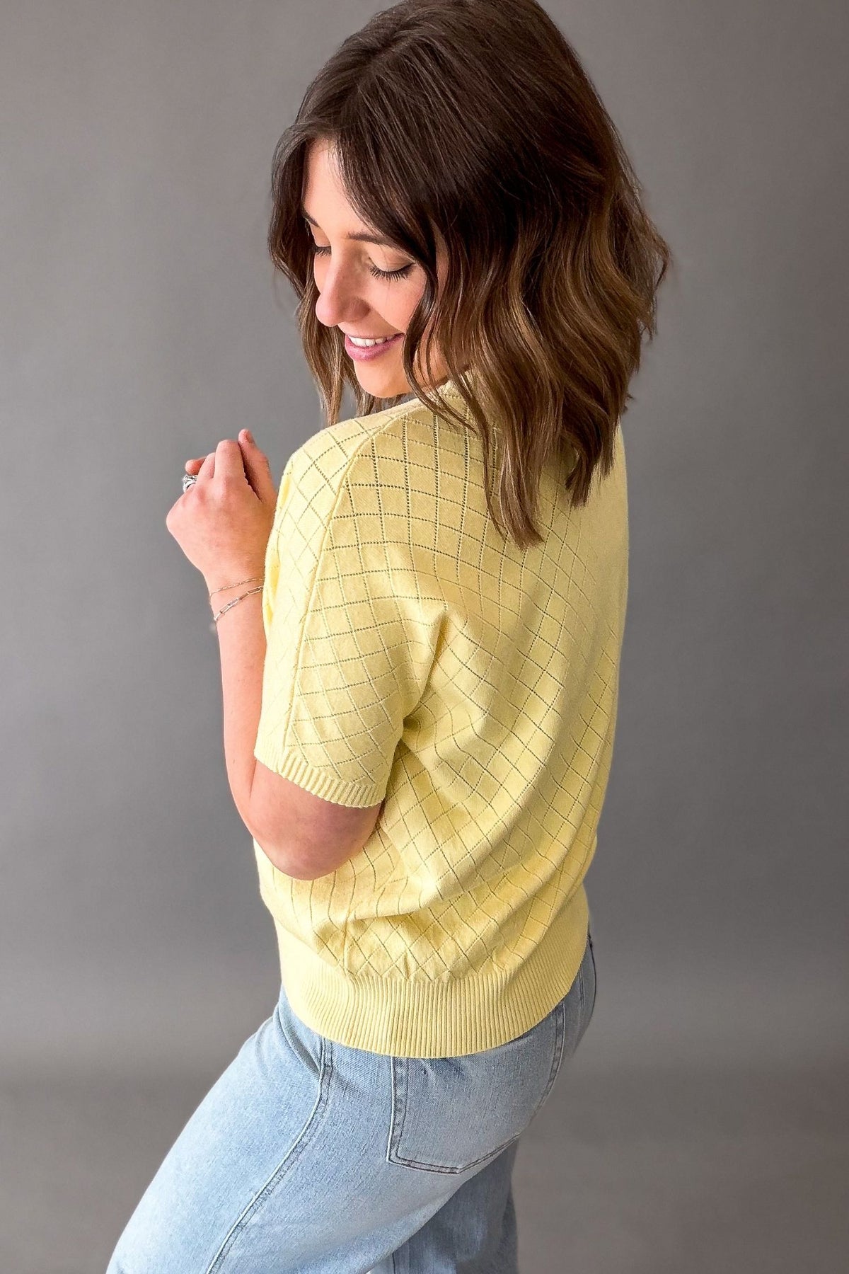 Woman wearing a yellow short sleeve and blue jeans against a gray background