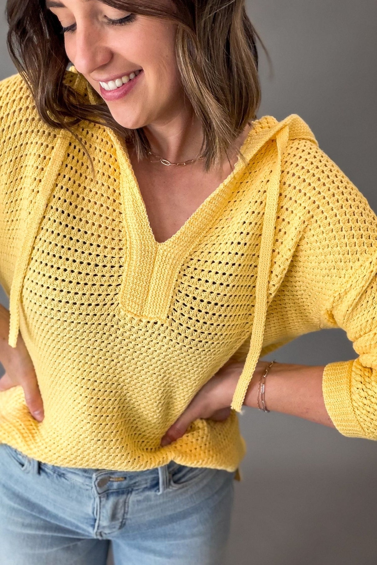 Woman wearing a yellow crochet top against a gray background
