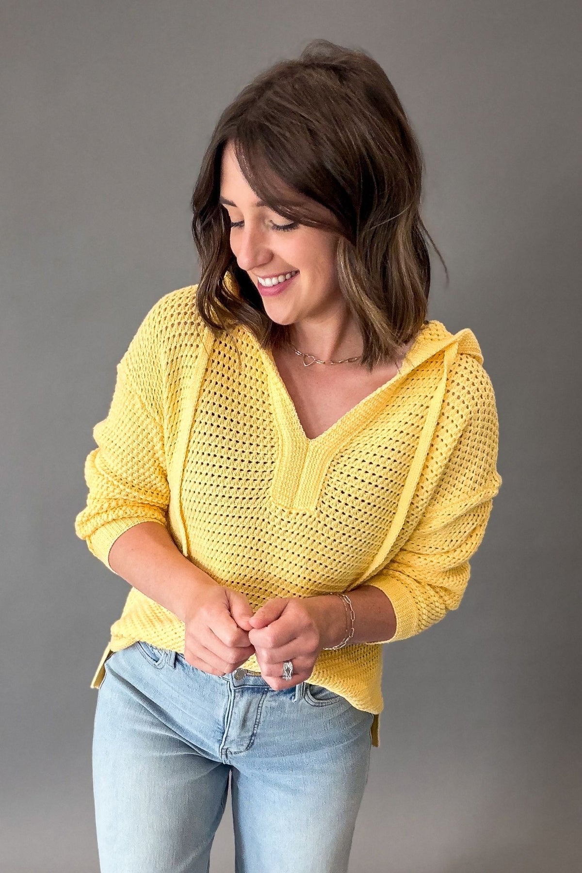 Woman wearing a yellow knitted sweater and light blue jeans against a gray background