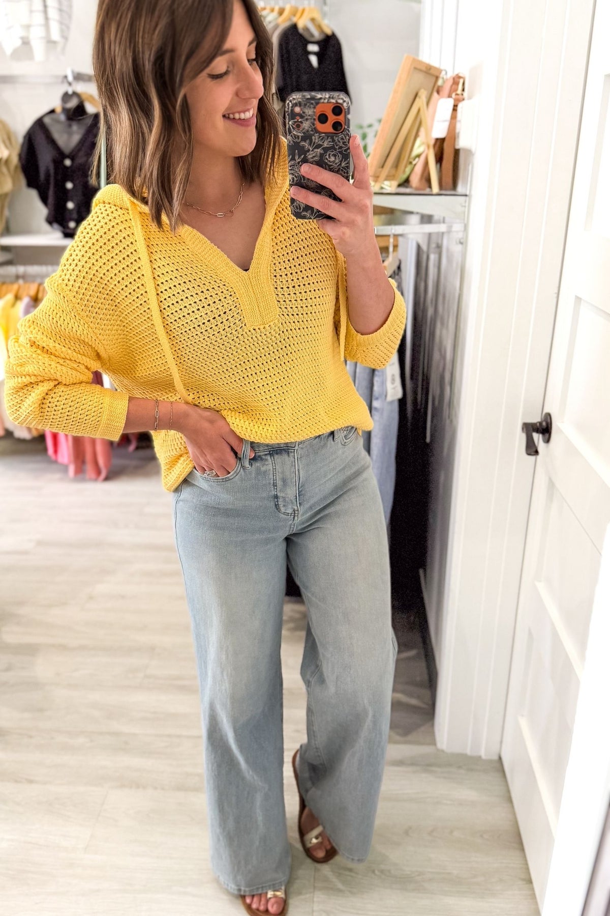 Woman taking a mirror selfie wearing a yellow sweater and light blue jeans in a room.
