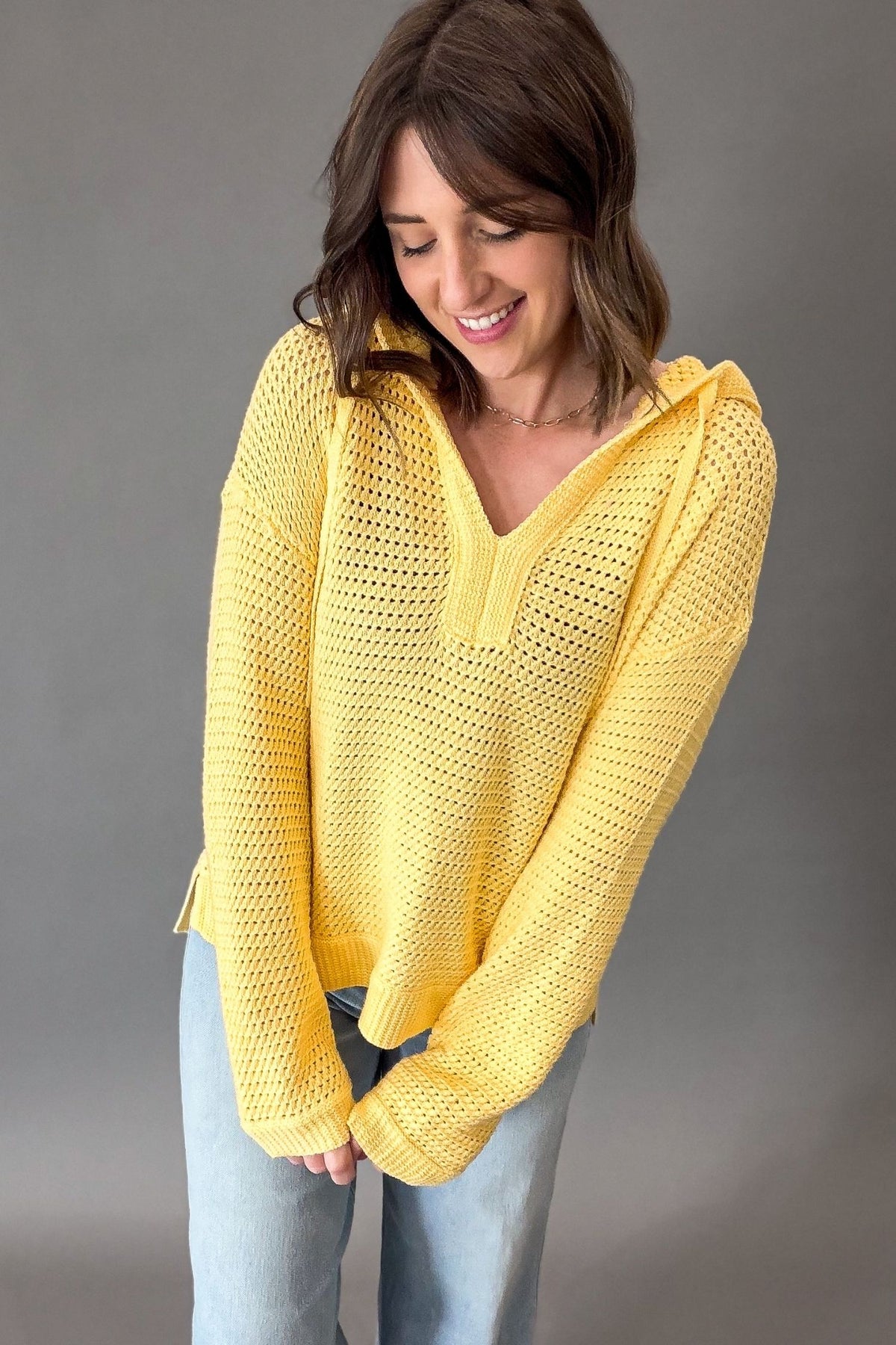 Woman wearing a yellow crochet hoodie against a gray background