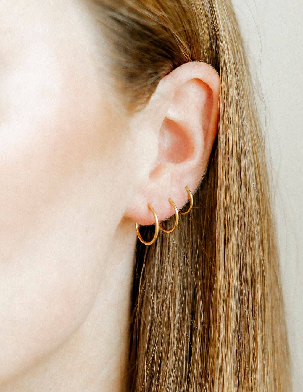 Close-up of an ear wearing gold hoop earrings with a neutral background