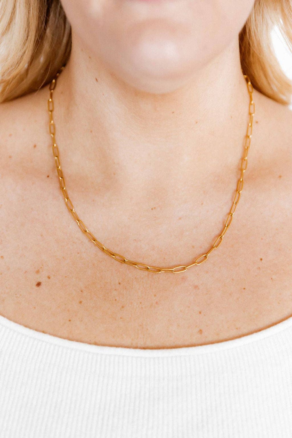 Gold chain necklace on a person wearing a white top